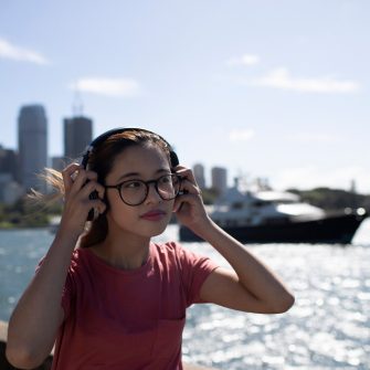 Female student putting on headphones in front of Sydney harbour skyline